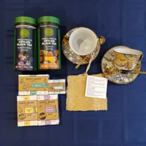 Assorted tea boxes and bath products laid out on a blue table: two green tea tins, soap bars, a loofah, and two decorative teacups with saucers on a blue cloth.